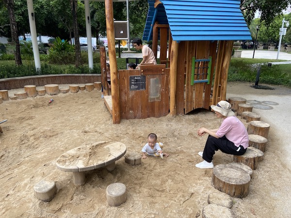 幼兒在沙池體驗感官遊戲，家長可坐在周邊的原木木椅上，方便照顧。