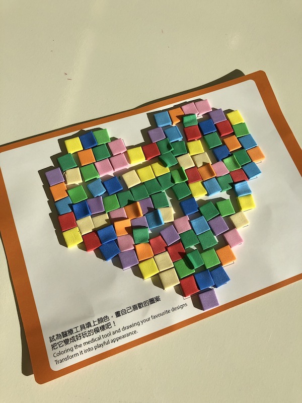 小朋友把心型圖案卡貼滿七色繽紛，向醫院遊戲師送上滿心感激！