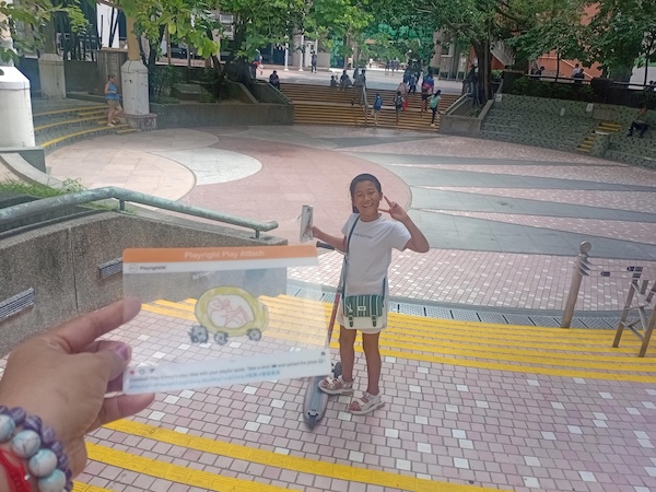 腳踏滑板車的Alexis喜歡和母親四處遊玩，途中更不忘以QQ card打卡影相，你可知道這是甚麼地方？